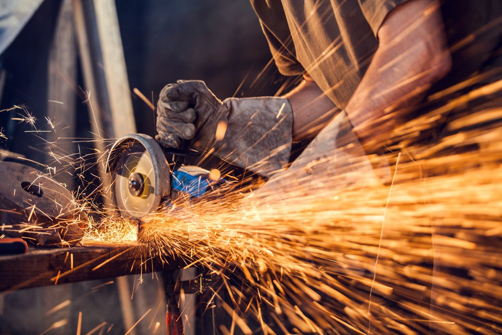 Sparks fly as a worker uses a handheld grinder to shape metal during fabrication