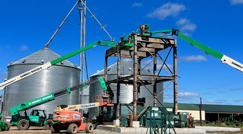 Multiple boom lifts supporting a rigging crew performing structural work on a steel platform at a grain processing facility.
