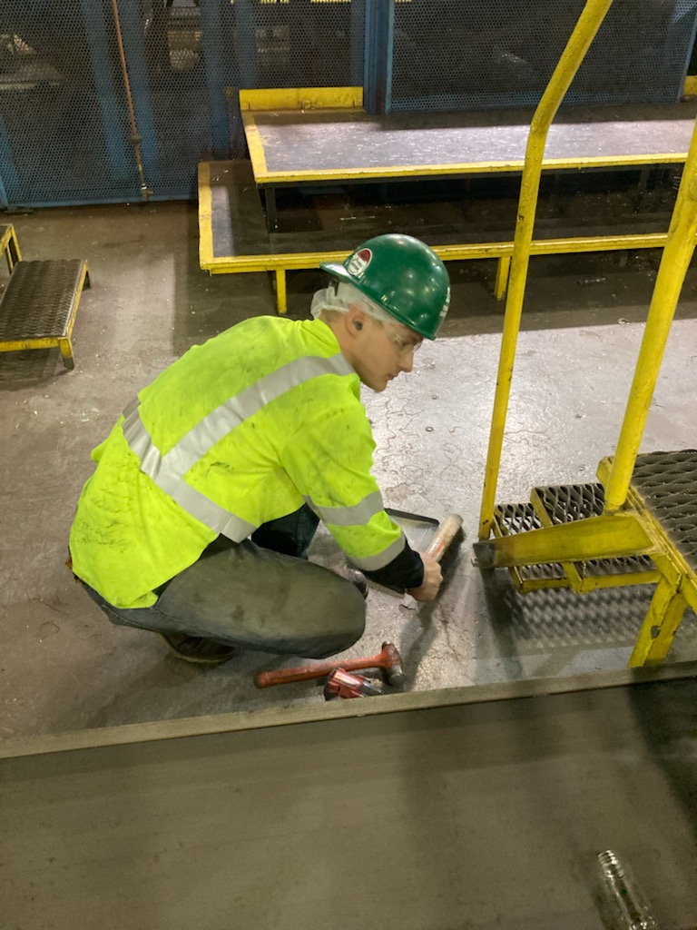A Lovegreen millwright in PPE working on a platform base with hand tools inside an industrial facility.