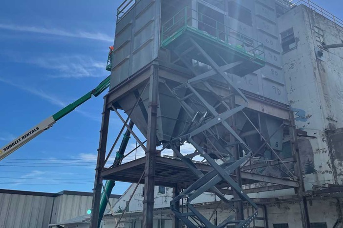 Millwright accessing a large elevated hopper using a boom lift for structural repair or maintenance work.