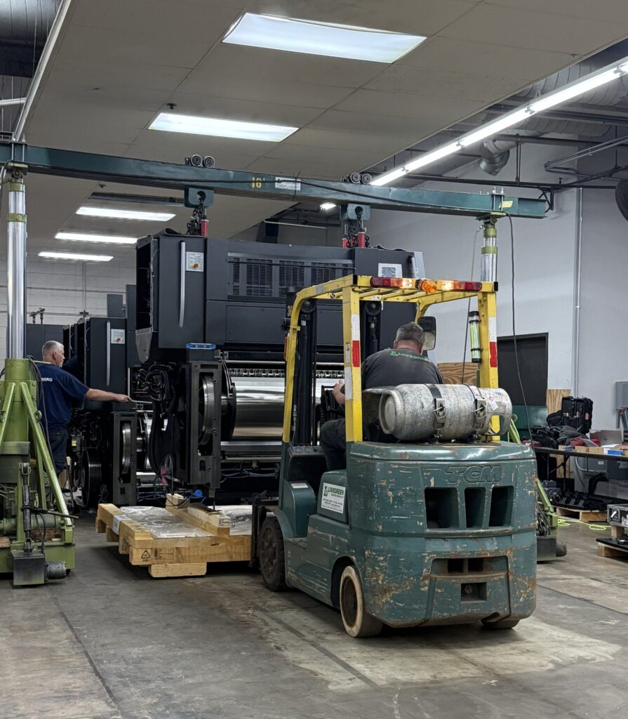 Lovegreen millwrights performing machinery rigging using a forklift and gantry system to position a large industrial press for installation.
