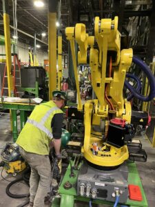 Millwright installing industrial robotic arm during automated equipment setup in manufacturing plant.